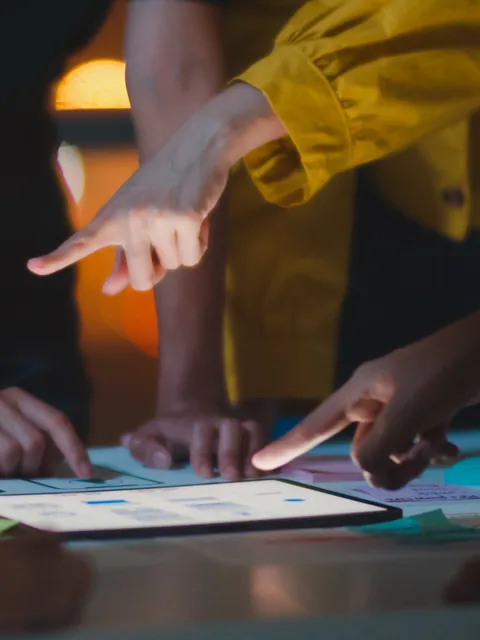 Mãos apontando para um tablet durante uma reunião — imagem ilustrativa